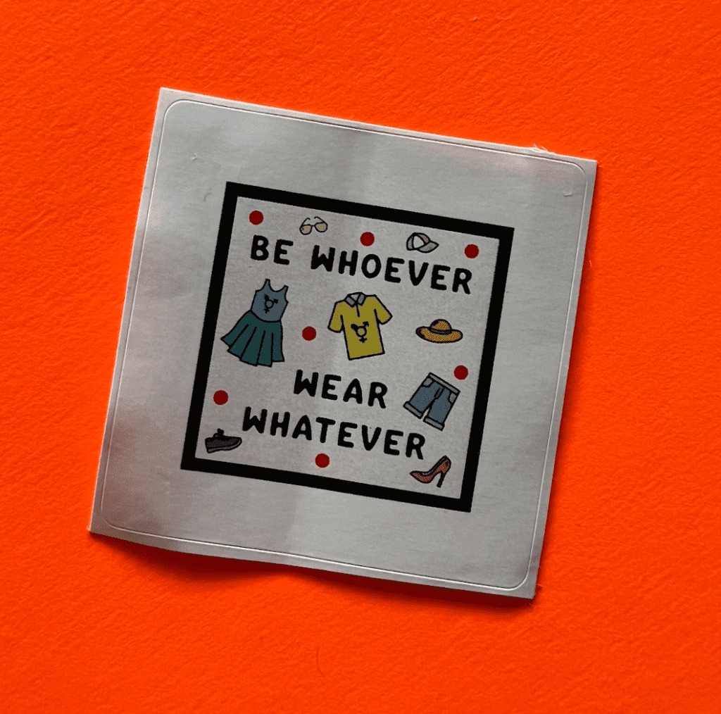 A white sticker on an orange background. The words read Be whoever wear whatever, and are surrounded by cartoon doodles of clothes