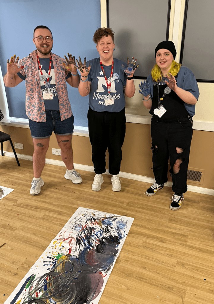 Three people with paint on their hands, faces and legs smiling